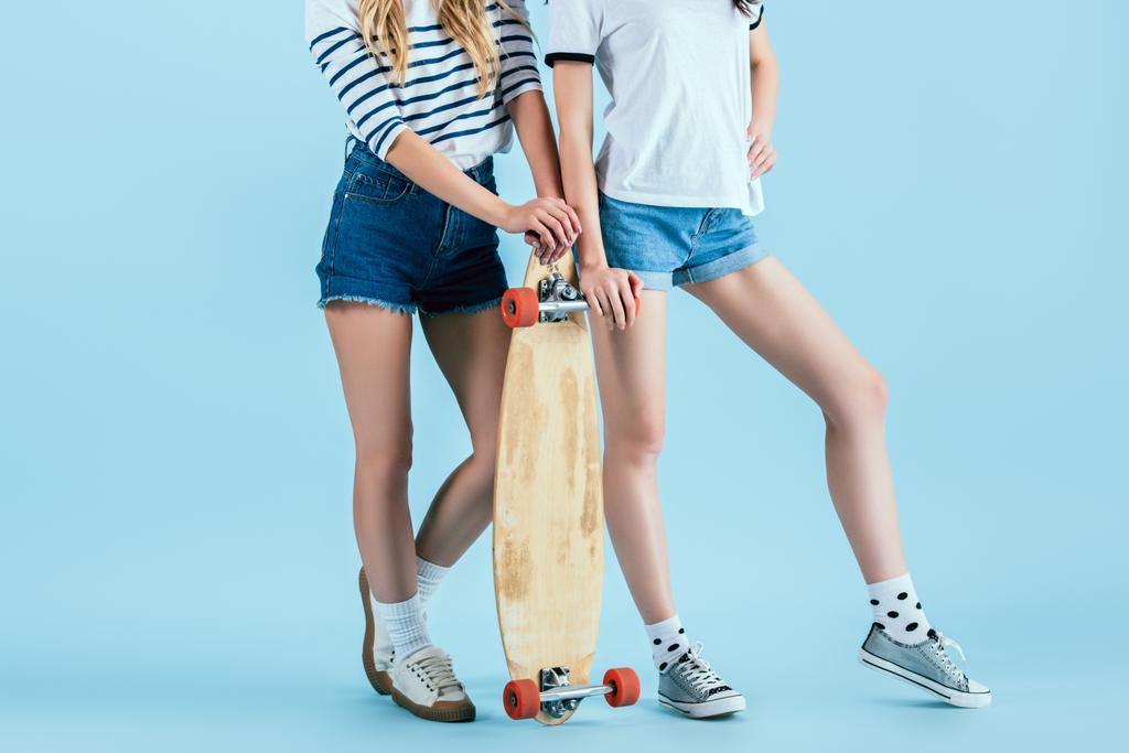 Cropped view of two girls posing with longboard on blue background - Photo, Image