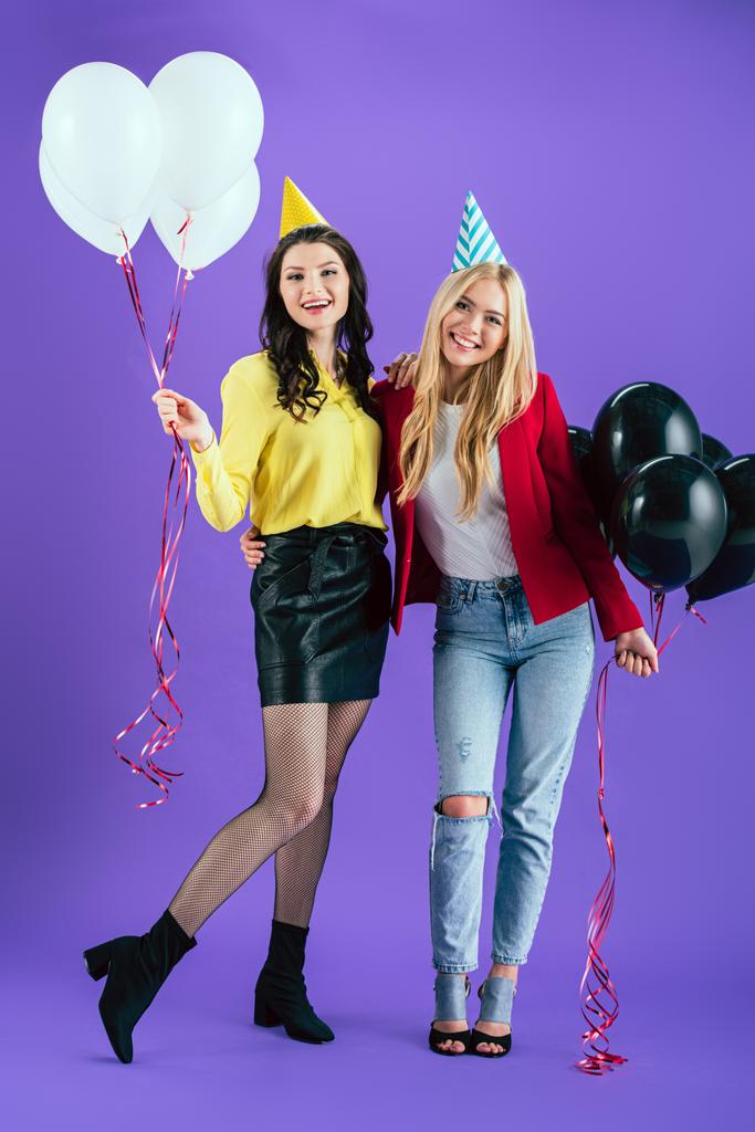 Studio shot van lachende meisjes met ballonnen omarmen op paarse achtergrond - Foto, afbeelding