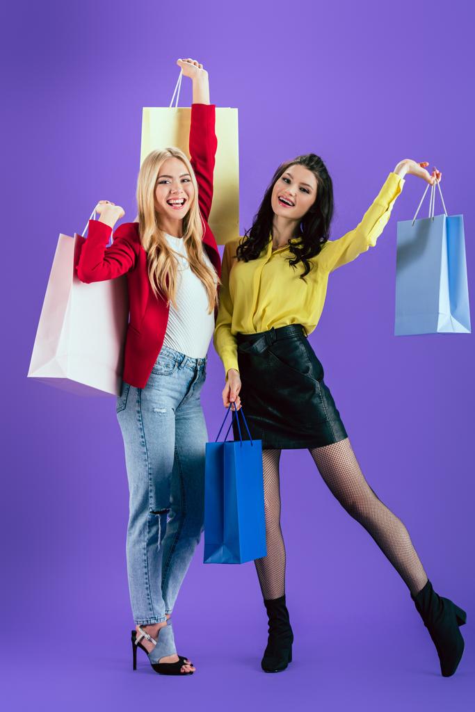 紫色の背景に買い物袋でポーズをとって幸せな若い女性 - 写真・画像