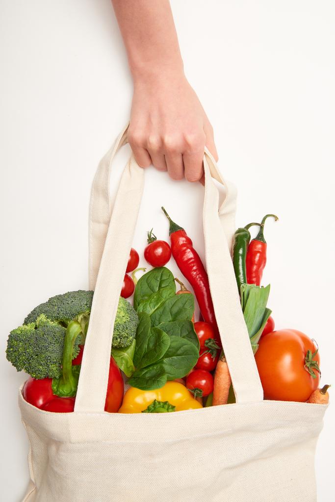 Vue recadrée d'une femme tenant un sac écologique avec des légumes sur fond blanc
 - Photo, image
