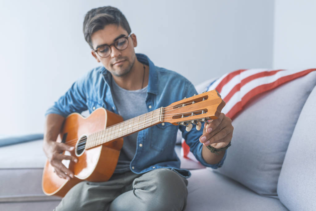 Portrait of young man sitting on sofa and playing guitar - Photo, Image