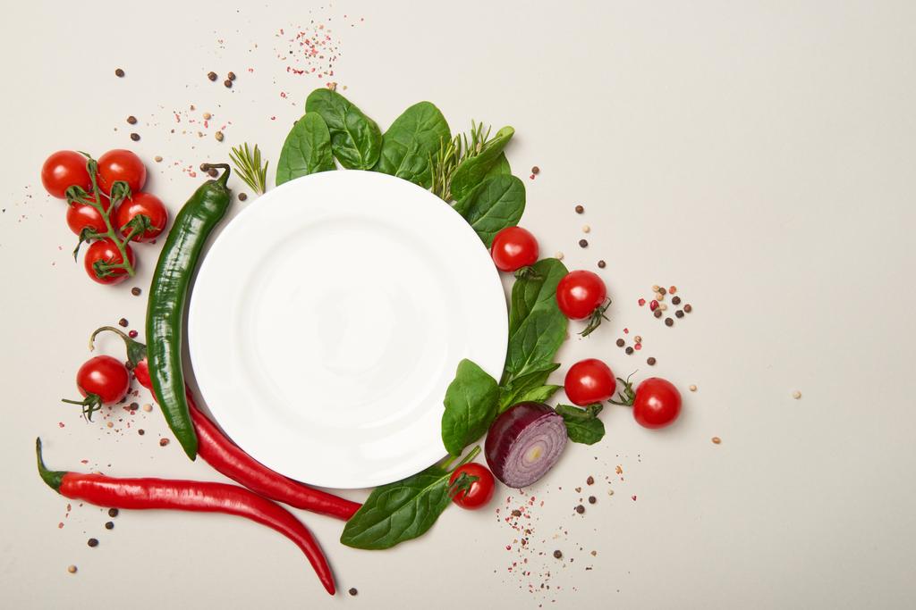Вид сверху на белую тарелку, овощи и специи на сером фоне
 - Фото, изображение