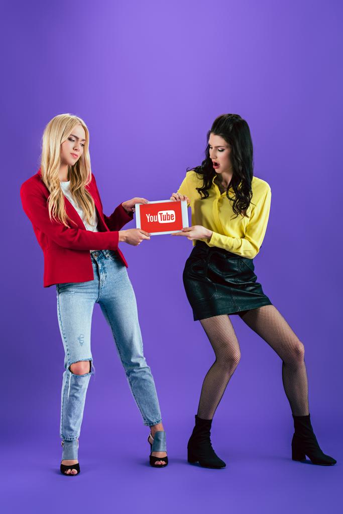 Unhappy girls holding digital tablet with youtube app on screen on purple background - Photo, Image