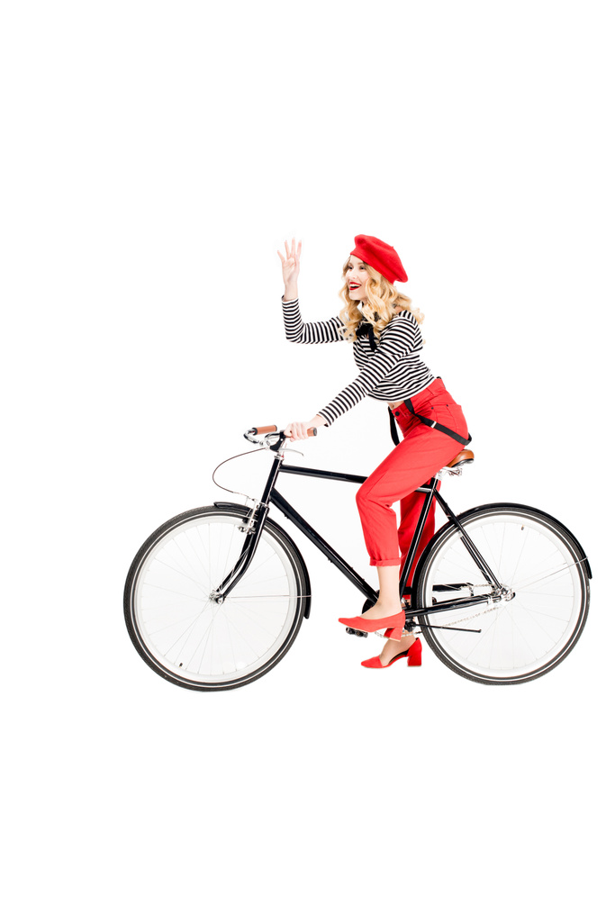 glückliche Frau in roter Baskenmütze winkt Hand beim Fahrradfahren isoliert auf weißem Grund  - Foto, Bild