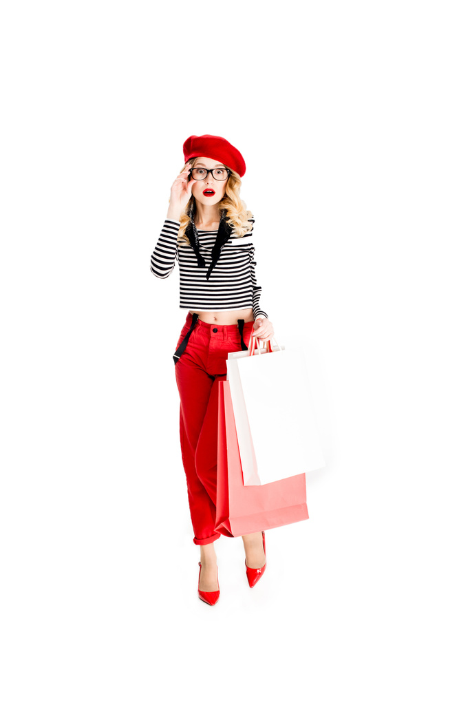 donna sorpresa in occhiali e berretto rosso con borse della spesa isolate su bianco
  - Foto, immagini