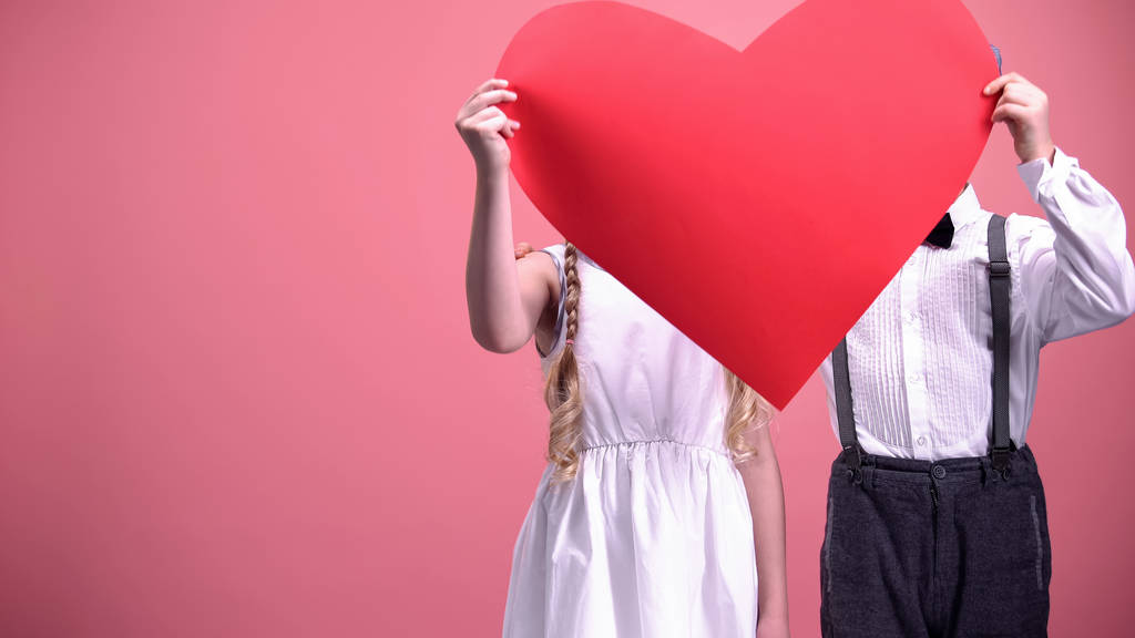 Un par de niños románticos escondidos detrás de un corte de corazón rojo y besos, primer amor
 - Foto, Imagen
