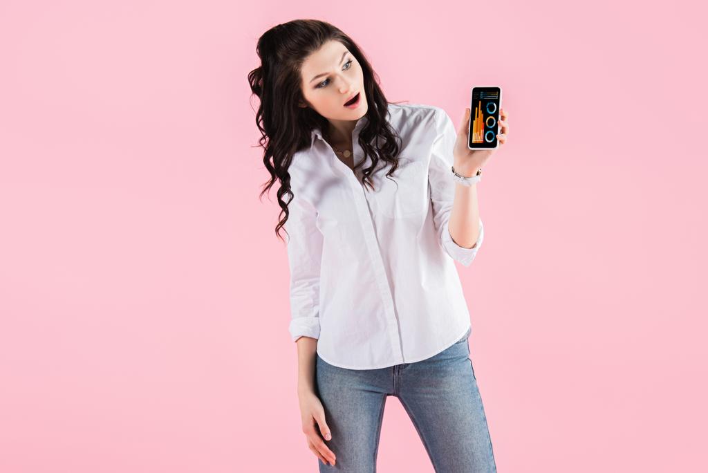 geschokt vrouw toont smartphone met infographic op scherm, geïsoleerd op roze - Foto, afbeelding