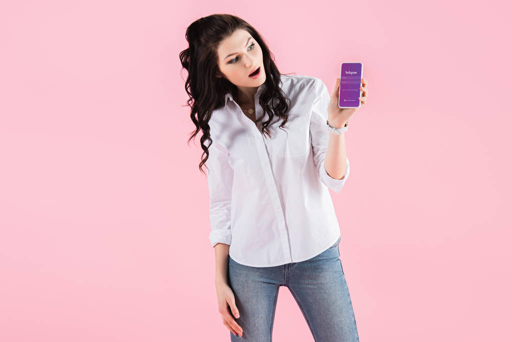 chica impactada mostrando teléfono inteligente con aplicación instagram en la pantalla, aislado en rosa
 - Foto, imagen