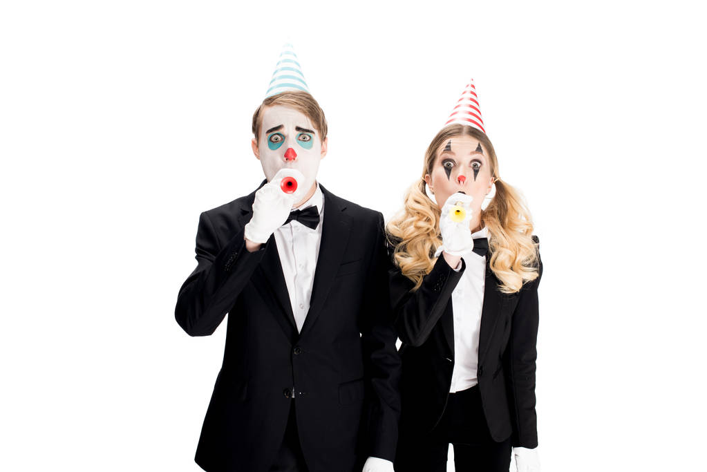 Пара клоунов в костюмах, дующих в праздничные вентиляторы, изолированные на белом
  - Фото, изображение