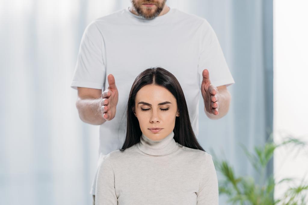 cropped shot of bearded healer doing reiki therapy session to young woman with closed eyes - Photo, Image