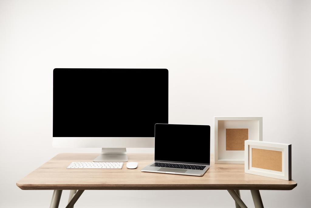 робоче місце з фоторамками, настільним комп'ютером і ноутбуком з копіювальним простором на дерев'яному столі ізольовано на білому
 - Фото, зображення