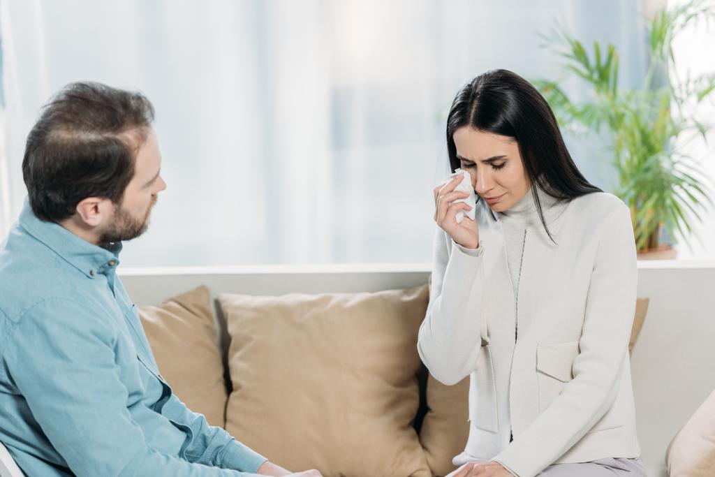 professional psychotherapist looking at young female patient crying on couch - Photo, Image