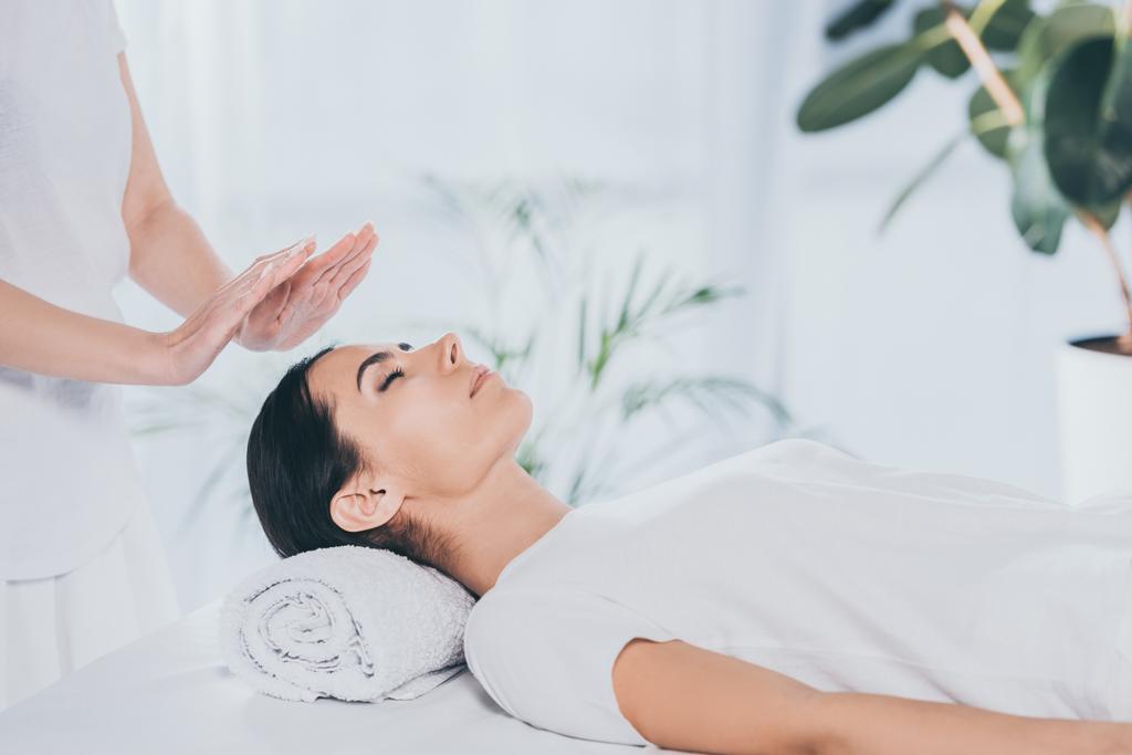 cropped shot of peaceful young woman with closed eyes receiving reiki treatment on head  - Photo, Image