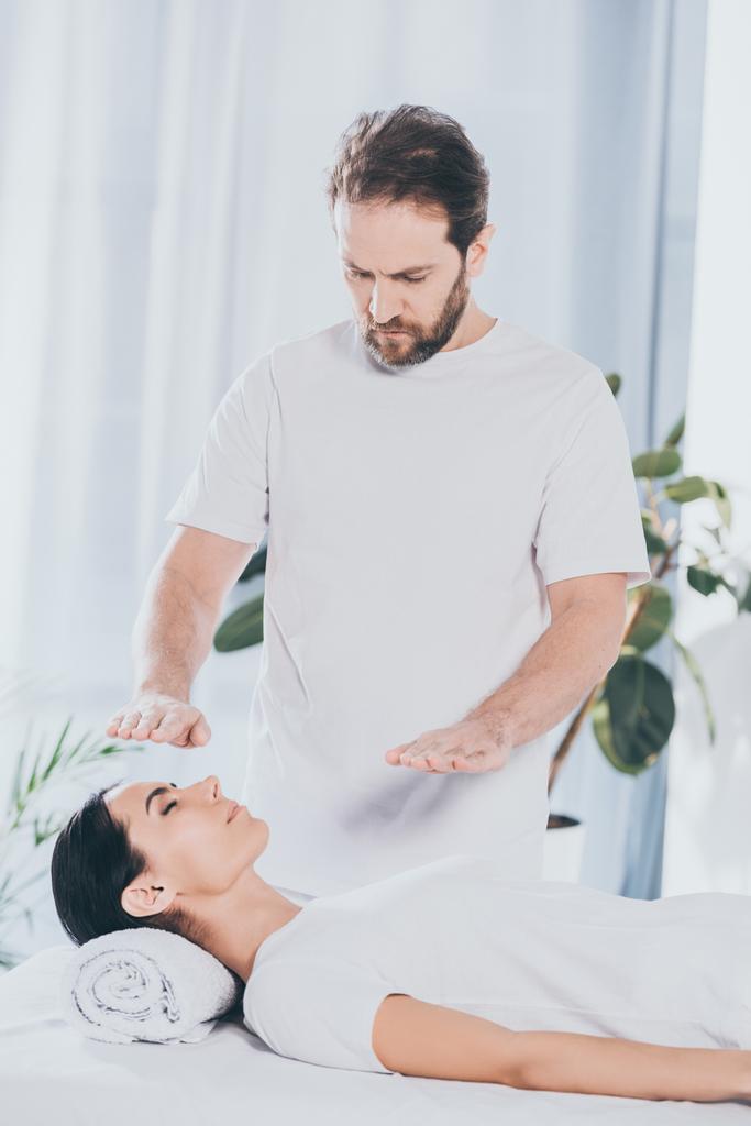 bearded healer doing reiki treatment session to young woman with closed eyes - Photo, Image