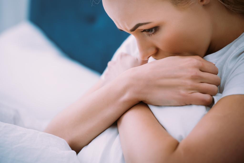 enfoque selectivo de la mujer estresada sosteniendo la manta mientras está acostada en la cama en casa
 - Foto, imagen