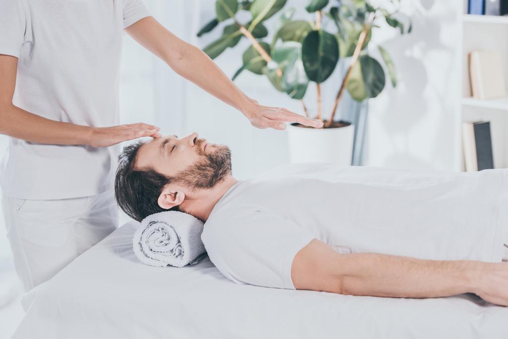 cropped shot of reiki healer doing treatment session to calm bearded man with closed eyes - Photo, Image