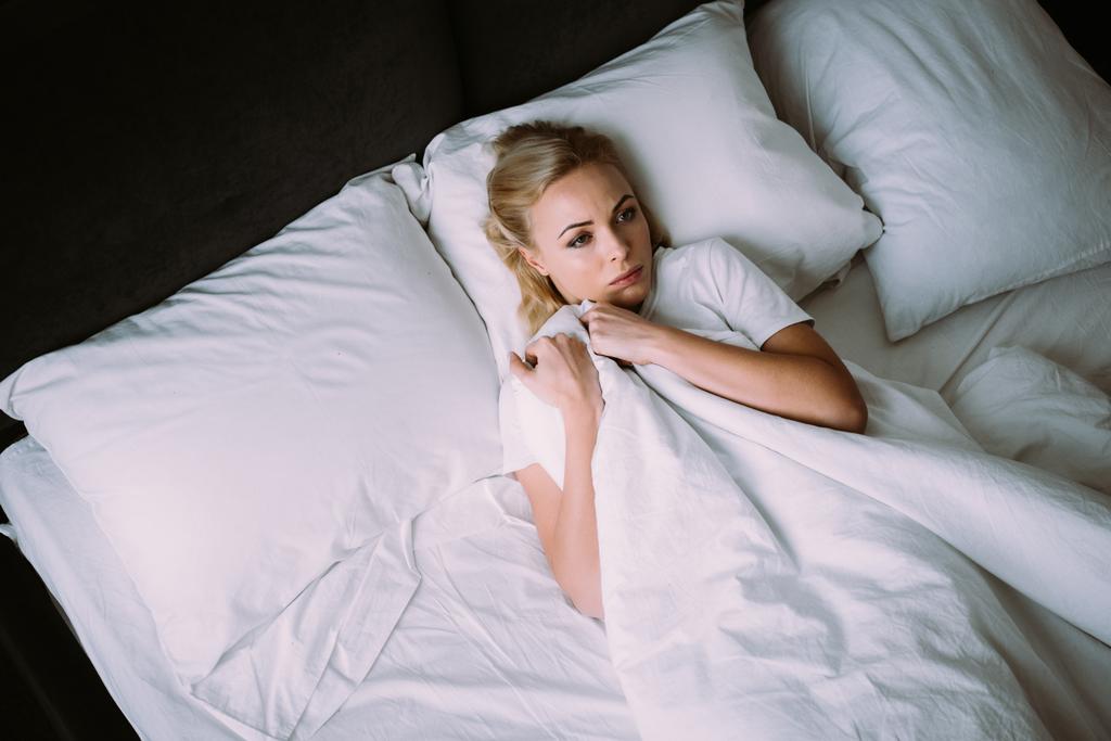 mujer asustada sosteniendo la manta y acostada en la cama en casa
 - Foto, imagen