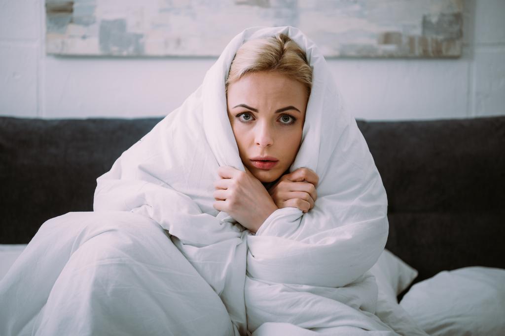 mujer asustada cubierta de manta mirando a la cámara en la cama
  - Foto, imagen
