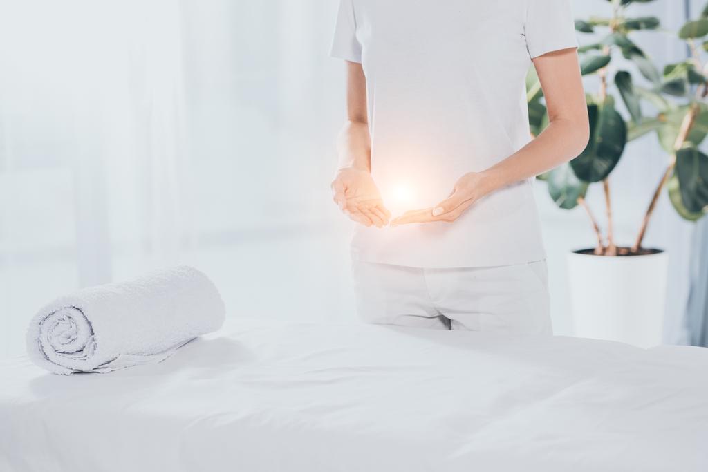 sezione centrale del guaritore reiki con energia luminosa nelle mani in piedi vicino al tavolo da massaggio bianco
  - Foto, immagini