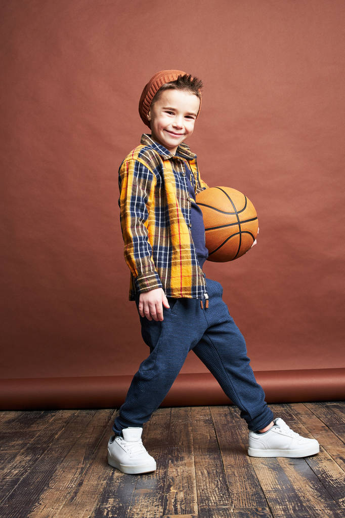 Stijlvolle jongen spelen basketbal. Studio opname, bruine achtergrond  - Foto, afbeelding