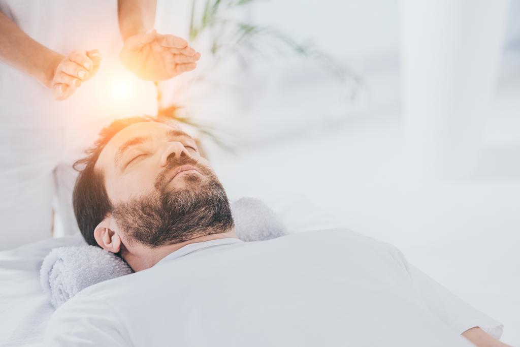 calm bearded man with closed eyes receiving reiki healing session  - Photo, Image