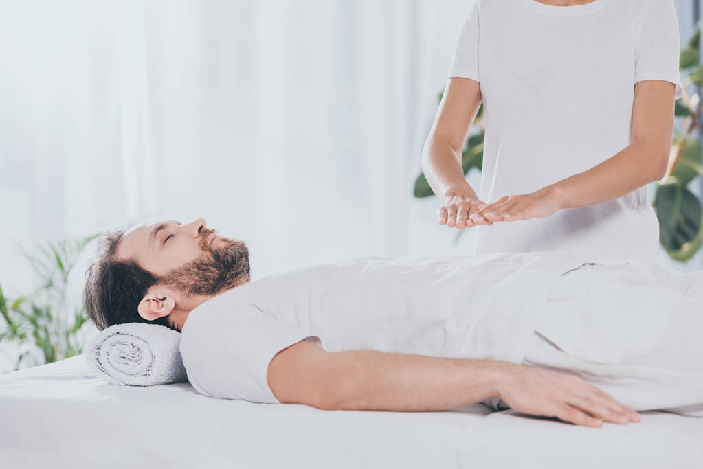 plan recadré d'homme barbu calme avec les yeux fermés couché sur la table de massage et recevant un traitement reiki
 - Photo, image