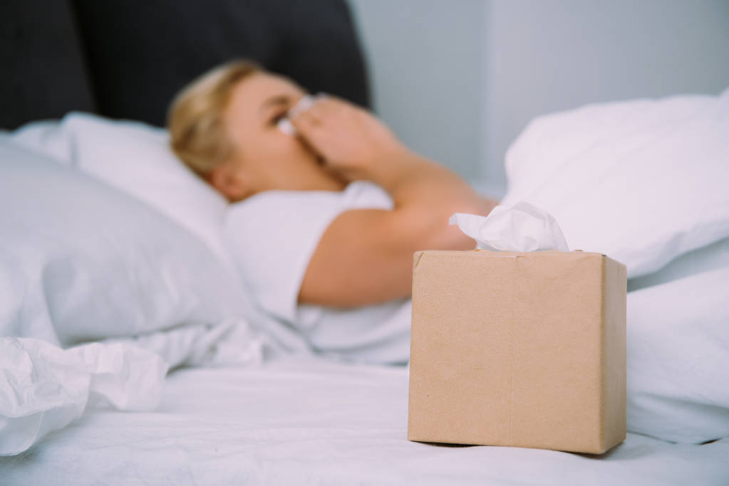 Selektywny fokus pudełko na chusteczki z kobieta ocierając łzy w łóżku na tle - Zdjęcie, obraz