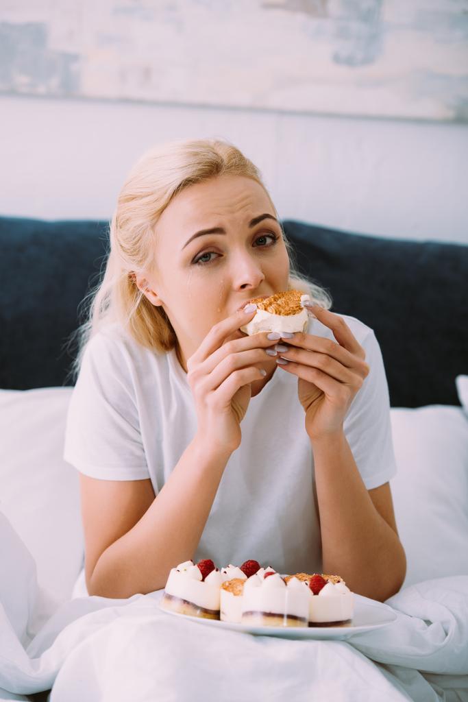 zdenerwowana Kobieta w piżamie, patrząc na kamery i jedzenie ciasto w łóżku sam - Zdjęcie, obraz