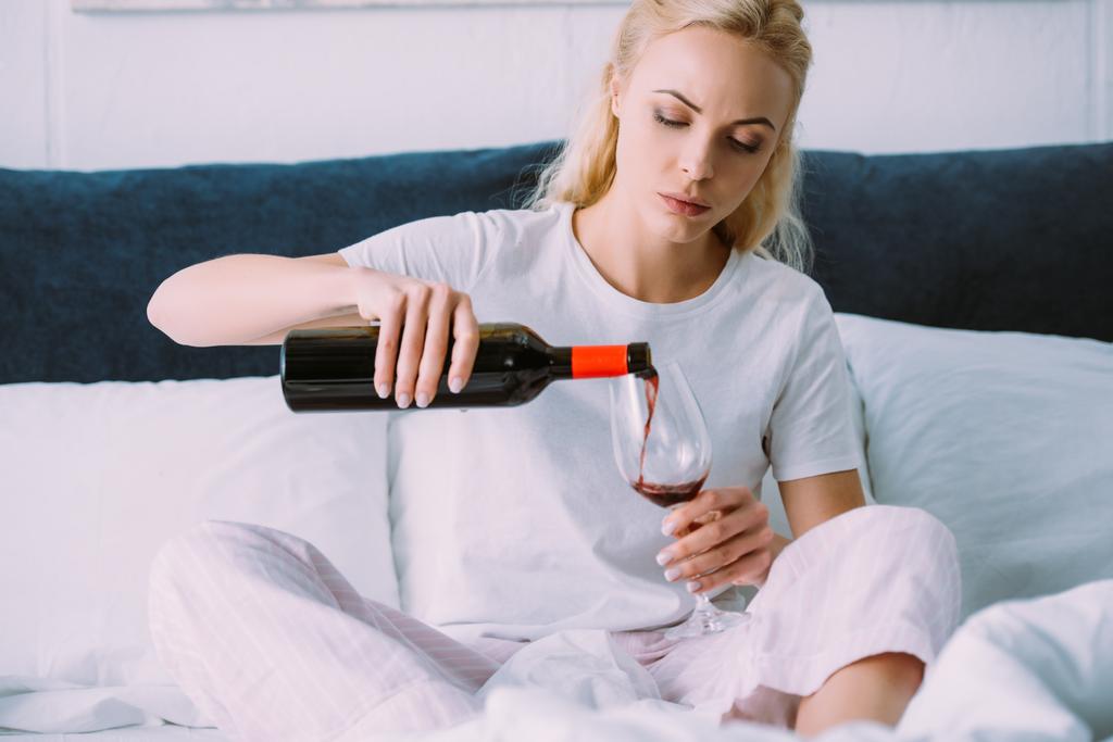 λυπημένη γυναίκα στο πιτζάμες έκχυση κόκκινο κρασί στο κρεβάτι στο σπίτι - Φωτογραφία, εικόνα