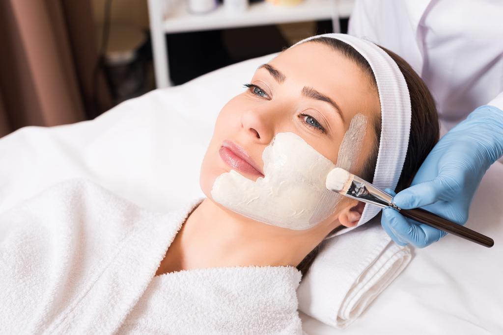 αισθητικός εφαρμογή καλλυντικών μάσκα στο πρόσωπο γυναίκας μέρος με καλλυντικά βούρτσα στο σαλόνι ομορφιάς - Φωτογραφία, εικόνα