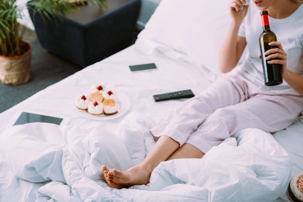 vista recortada de la mujer con pasteles y botella de vino celebrando cumpleaños en la cama solo
 - Foto, imagen