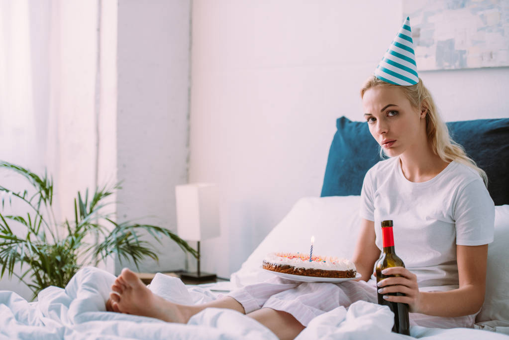 järkyttynyt nainen pullon viiniä ja kakkua juhlii syntymäpäivää sängyssä yksin
 - Valokuva, kuva