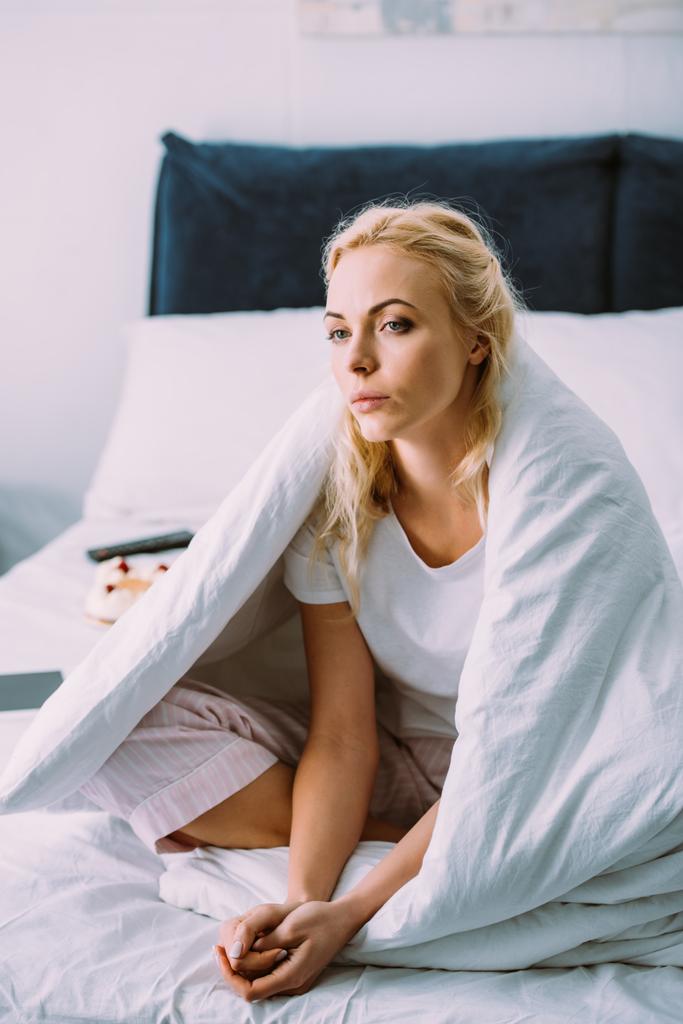 вибірковий фокус сумної самотньої жінки, покритої ковдрою, сидить на ліжку вдома
 - Фото, зображення