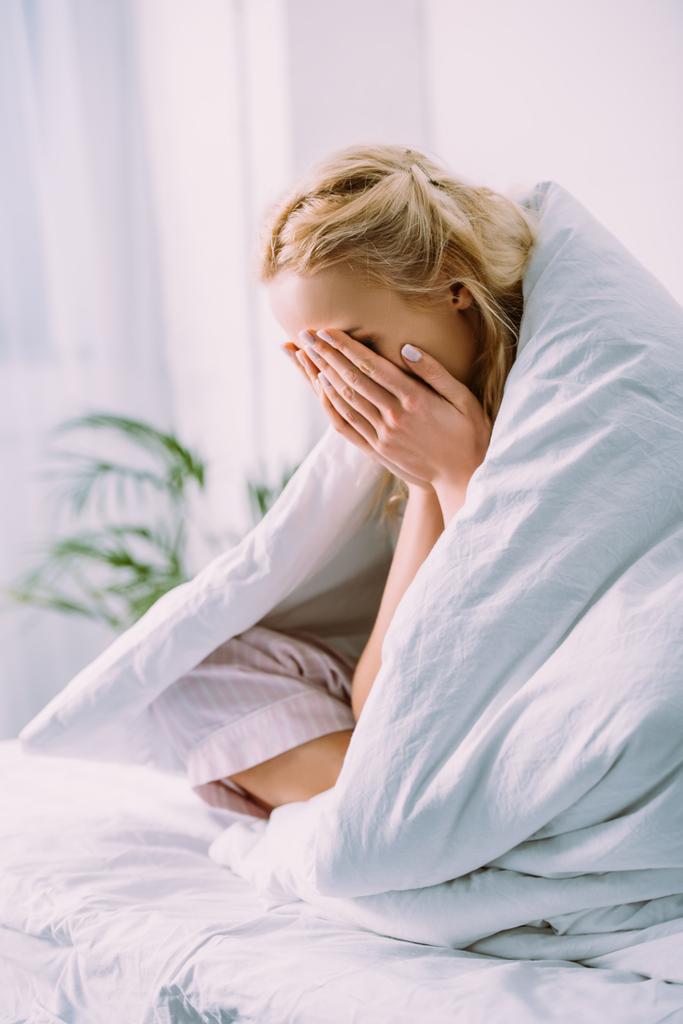 жінка в ковдрі покриває обличчя руками і плаче в ліжку вдома
  - Фото, зображення
