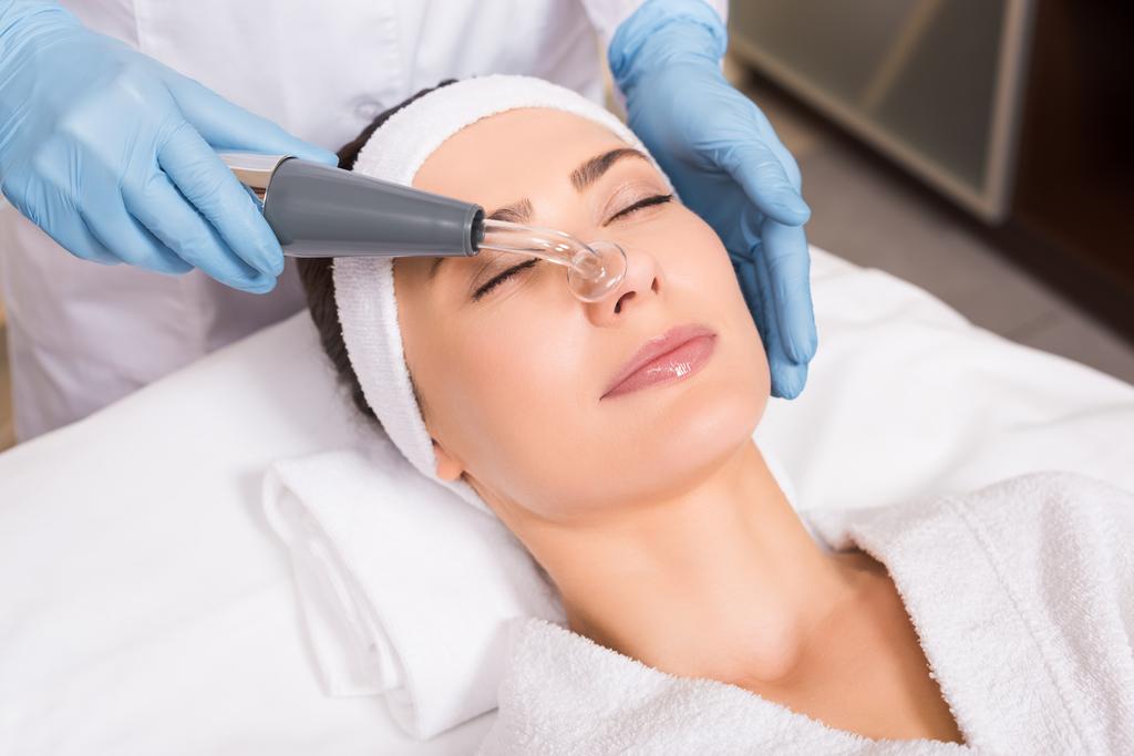 esteticista fazendo fisioterapia whith darsonvalization equipamentos no rosto da mulher no salão de beleza
 - Foto, Imagem