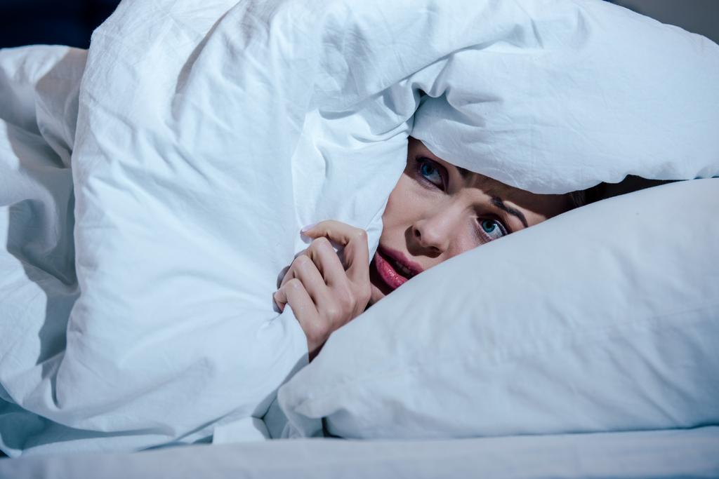 mulher assustada escondendo atrás cobertor no quarto em casa
 - Foto, Imagem