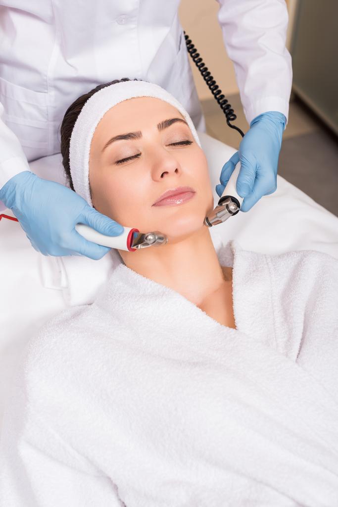 esteticista fazendo massagem com equipamento para mulher no rosto no salão de beleza
 - Foto, Imagem