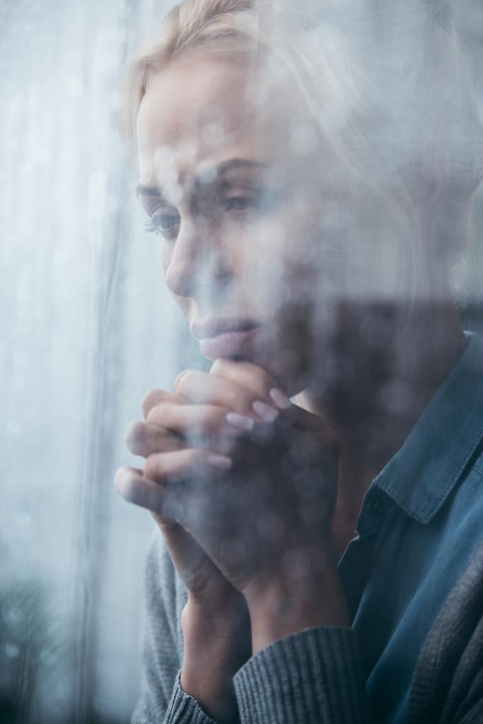 smutny dorosłej kobiety z założonymi rękoma w domu przez okno z deszczu - Zdjęcie, obraz