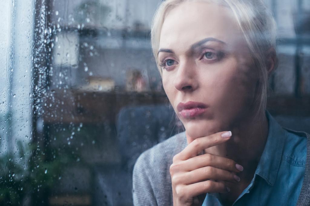 sad thoughtful adult woman touching face at home through window with raindrops - Photo, Image