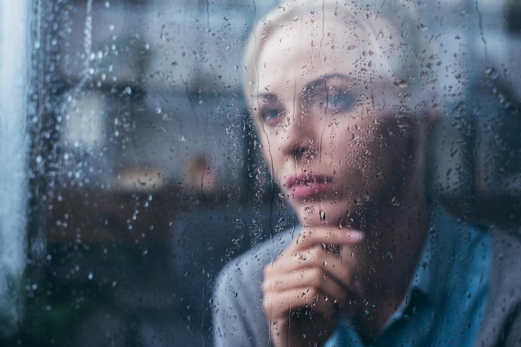 Грустная задумчивая взрослая женщина, прикасающаяся лицом к дому через окно каплями дождя
 - Фото, изображение