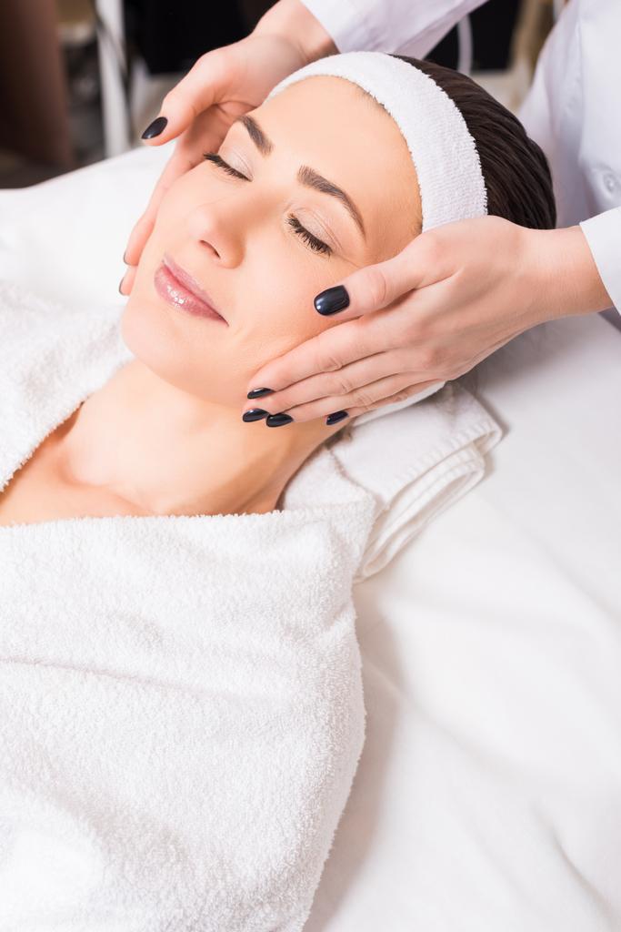schoonheidsspecialiste handmatige gezicht massage geven vrouw liggen op badjas en hairband op de salon van de schoonheid - Foto, afbeelding