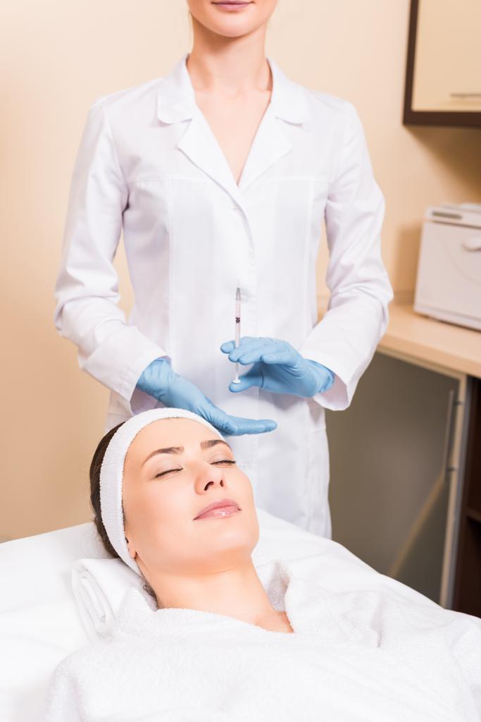 mulher deitada na mesa de massagem enquanto esteticista prepara a injeção em seringa no salão de beleza
 - Foto, Imagem
