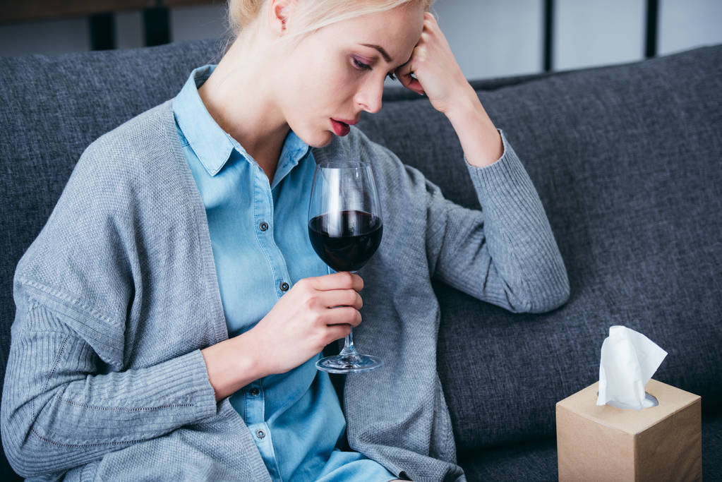 järkyttynyt nainen istuu lasi punaviiniä ja kudosta laatikko kotona
 - Valokuva, kuva
