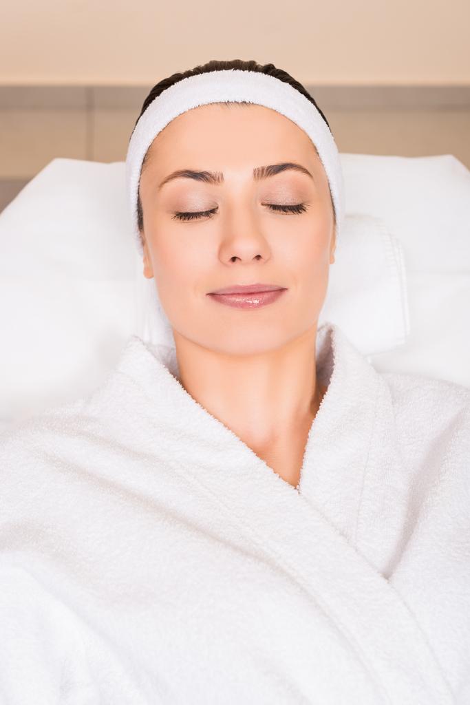 Draufsicht einer Frau im weißen Bademantel mit geschlossenen Augen im Schönheitssalon - Foto, Bild