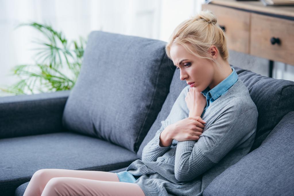 Traurige Frau in lässiger Kleidung sitzt zu Hause auf Couch - Foto, Bild