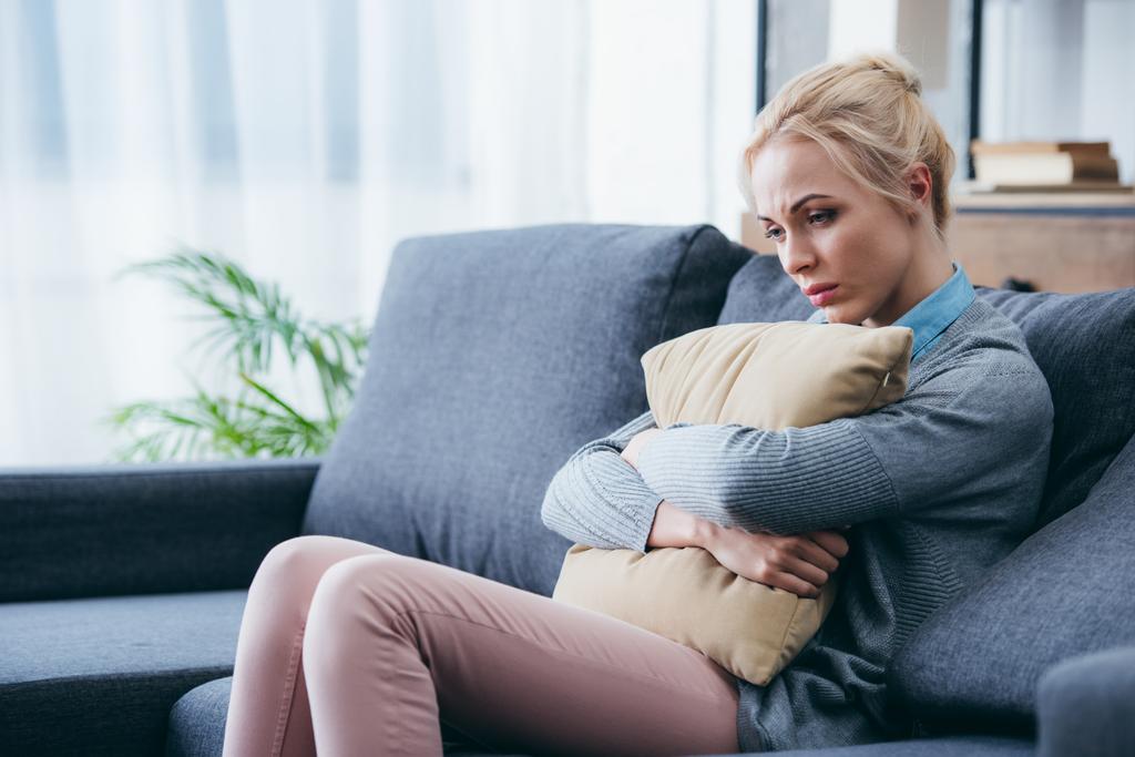 Depressive Frau sitzt auf Sofa und hält Kissen zu Hause - Foto, Bild