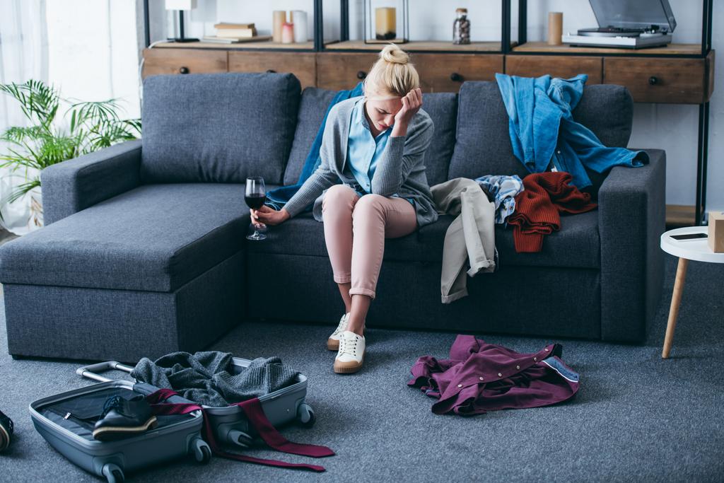 mujer deprimida sentada con un vaso de vino tinto y llorando mientras empaca en la sala de estar después de romper con su novio
 - Foto, Imagen