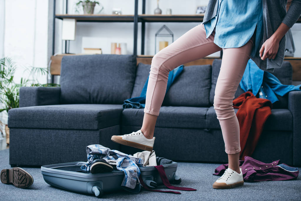 oříznutý pohled ženy tlačí oblečení v kufru s nohou po rozchodu s přítelem - Fotografie, Obrázek