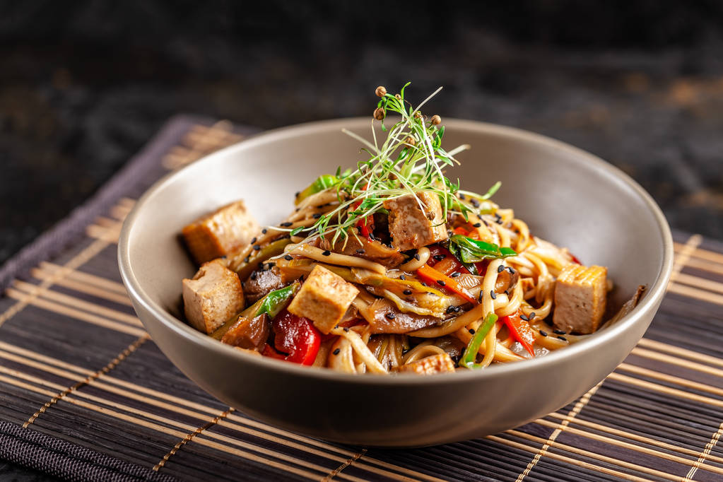 Η έννοια της ιαπωνικής κουζίνας. Κινεζικά noodles με κοτόπουλο, λαχανικά σχάρας και τόφου σε σάλτσα unagi. Σερβίρει ασιατικά πιάτα στο εστιατόριο σε ένα πιάτο σε ένα χαλί μπαμπού. Το top view, αντίγραφο χώρου - Φωτογραφία, εικόνα