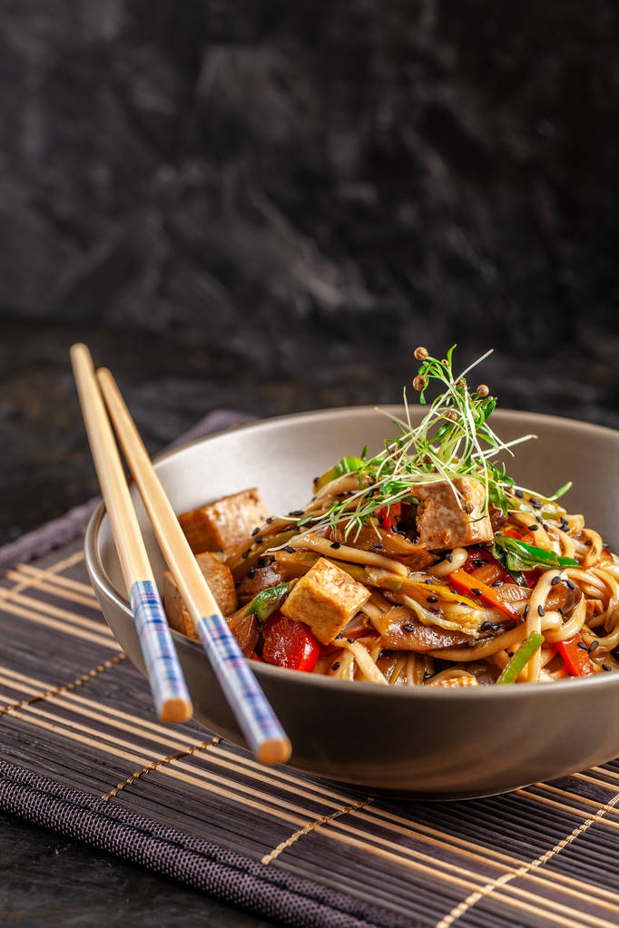 das Konzept der japanischen Küche. Chinesische Nudeln mit Huhn, gegrilltem Gemüse und Tofu in Unagi-Sauce. serviert asiatische Gerichte im Restaurant in einem Teller auf einer Bambusmatte. Ansicht von oben, Kopierraum - Foto, Bild